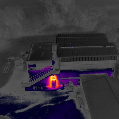 Inspection thermique par drone d’un bâtiment industriel : point chaud visible sur la façade près de l’escalier extérieur.